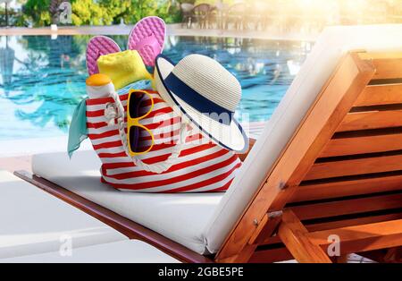 Strandtasche mit Accessoires auf Sonnenliege in der Nähe des Swimmingpools im Luxusresort Stockfoto