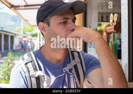 Der junge Mann in der Mütze legte seine Hand auf sein Kinn und schaut nachdenklich an die Bar. Sommerurlaub Entspannung und Erholung. Stockfoto