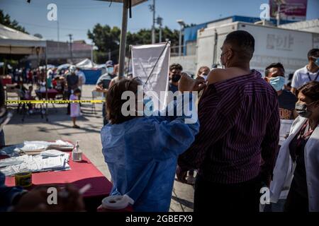 Tijuana, Mexiko. August 2021. Ein Gesundheitsmitarbeiter verabreicht einem Migranten außerhalb des Grenzübergangs von El Chaparral eine Corona-Impfung. Die Impfkampagne wurde vom Gesundheitsministerium des mexikanischen Bundesstaates Baja California organisiert. Rund 500 Migranten, die im improvisierten Lager am Grenzübergang lebten, sollten den Corona-Impfstoff von Pfizer-BioNTech erhalten. Kredit: Stringer/dpa/Alamy Live Nachrichten Stockfoto