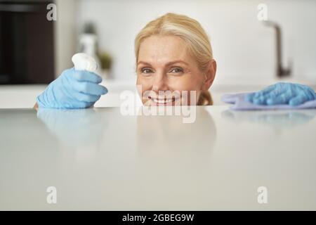Porträt einer glücklichen blonden Hausfrau in Gummihandschuhen lächelnd an der Kamera, zufrieden mit den Ergebnissen der Reinigung in der Küche Stockfoto