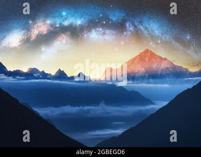 Milky Way Bogen und schneebedeckte Berge in niedrigen Wolken in der sternenklaren Nacht Stockfoto