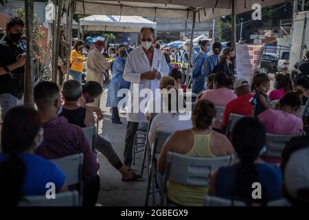 Tijuana, Mexiko. August 2021. Ein Arzt, der Mund und Nase bedeckt, beobachtet Migranten, die am Grenzpunkt von El Chaparral eine Corona-Impfung erhalten haben. Die Impfkampagne wurde vom Gesundheitsministerium des mexikanischen Bundesstaates Baja California organisiert. Rund 500 Migranten, die im improvisierten Lager am Grenzübergang lebten, sollten den Corona-Impfstoff von Pfizer-BioNTech erhalten. Kredit: Stringer/dpa/Alamy Live Nachrichten Stockfoto