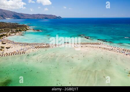 Luftaufnahme von Sonnenschirmen und Sonnenschirmen an einem schmalen Sandstrand, der von flachen Lagunen umgeben ist (Elafonisso Beach, Kreta, Griechenland) Stockfoto