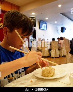 Ein kleiner Junge (9 Jahre), der mit Essstäbchen isst Stockfoto