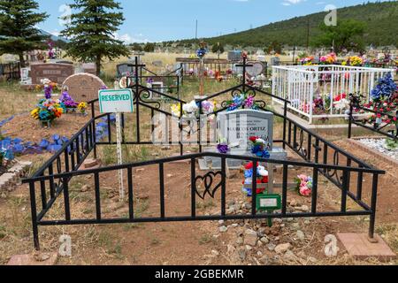 Cerro, New Mexico - EIN ländlicher Friedhof, auf dem Gräber mit Blumen und Fahnen geschmückt sind. Ein Begräbnisplatz ist reserviert. Stockfoto