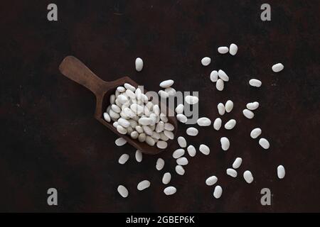 Weiße Kidney-Bohnen in Holzlöffel isoliert auf Holzhintergrund Nahaufnahme. Draufsicht. Stockfoto