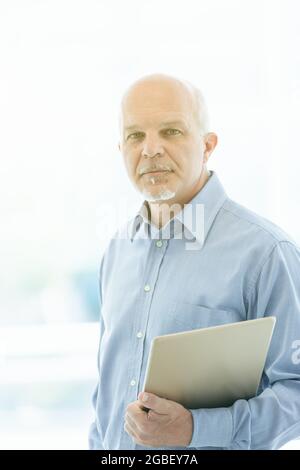 Ein nachdenklicher Geschäftsmann, der in einem High-Key-Bild mit Lichtern die Kamera anstarrt, während er mit einem Tablet unter seinem Arm steht Stockfoto