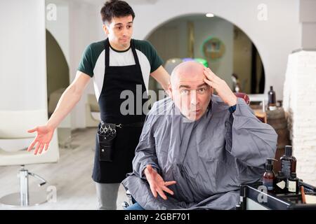 Unzufriedener Mann mit rasierten Kopf im Friseurladen Stockfoto