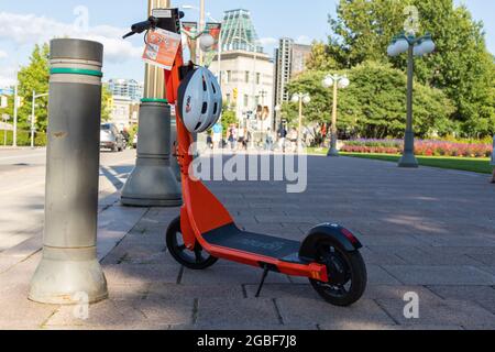 Ottawa, Kanada - 2. August 2021: Elektroroller mit Helm zur Miete auf der Straße. Orange E-Scooter auf dem Bürgersteig in der Innenstadt geparkt Stockfoto