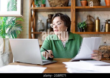 Eine reife Frau beim Ausfüllen von Dokumenten. Sie verwendet ein Online-Tutorial, um die Dokumentation korrekt auszufüllen. Stockfoto