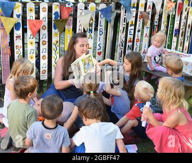 30. Juli 2021, Sachsen, Rötha/OT Mölbis: In der Kindertagesstätte Mölbiser Lämmchen malen und lesen Kinder mit ihrer Lehrerin Tina. Die Kindertagesstätte befindet sich direkt am Schlosspark und neben einer neu installierten Arkade. Die Arkade, ausgestattet mit überdachten Sitzgelegenheiten und Informationstafeln, ist eines der Projekte der Dorfentwicklungsgesellschaft, die den Schlosspark im Zentrum des Dorfes auf seine frühere Schönheit und mit barocken Elementen umgestalten will. Mölbis wurde in der DDR wegen der Umweltverschmutzung durch die Espenhai als das "dreckigste Dorf Europas" bekannt Stockfoto