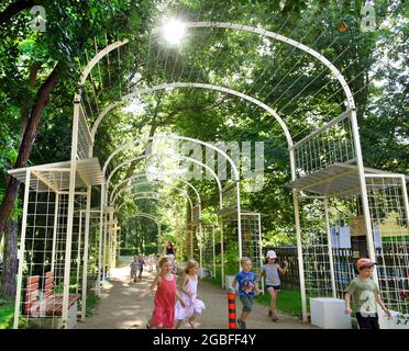 30. Juli 2021, Sachsen, Rötha/OT Mölbis: Im Schlosspark laufen Kinder der Kindereinrichtung Mölbiser Lämmchen durch die neu installierte Spielhalle. Die Arkade, ausgestattet mit überdachten Sitzgelegenheiten und Informationstafeln, ist eines der Projekte der Dorfentwicklungsgesellschaft, die den Schlosspark im Zentrum des Dorfes auf seine frühere Schönheit und mit barocken Elementen umgestalten will. Mölbis wurde in der DDR als das "dreckigste Dorf Europas" bekannt, weil die Umweltverschmutzung durch das Espenhain-Werk, das aus einer Schmelze, einer Kohlefabrik, einer Brikett f bestand, verursacht wurde Stockfoto