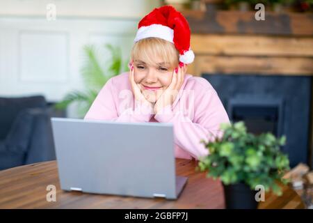 Fröhlich lächelnde junge Frau in Weihnachtsmütze vor dem Laptop-Monitor. Online-Treffen mit Freunden oder Familie am Vorabend von Weihnachten oder Neujahr. Stockfoto