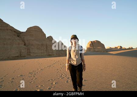asiatische Frau Reisende Backpacker zu Fuß in der Wüste bei Sonnenuntergang mit Yardang Landform im Hintergrund Stockfoto