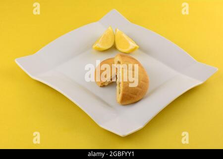 Griechische Zitronen-Shortbread-Pie-Hälften mit Zitronenscheiben auf weißem Snackteller auf gelbem Hintergrund Stockfoto