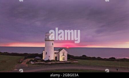 Hunstanton, Großbritannien. August 2021. Am 2. August 2021 erscheint am Horizont unter dunklen Wolken ein orangefarbener Schleier, während die Sonne hinter dem alten Leuchtturm von Hunstanton am Ende der Tageslichtstunden in Hunstanton, Norfolk, Großbritannien, untergeht.Quelle: Paul Marriott/Alamy Live News Stockfoto