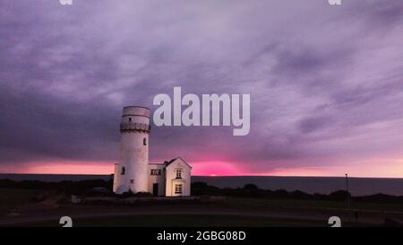 Hunstanton, Großbritannien. August 2021. Am 2. August 2021 erscheint am Horizont unter dunklen Wolken ein orangefarbener Schleier, während die Sonne hinter dem alten Leuchtturm von Hunstanton am Ende der Tageslichtstunden in Hunstanton, Norfolk, Großbritannien, untergeht.Quelle: Paul Marriott/Alamy Live News Stockfoto