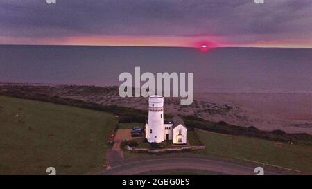 Hunstanton, Großbritannien. August 2021. Am 2. August 2021 erscheint am Horizont unter dunklen Wolken ein orangefarbener Schleier, während die Sonne hinter dem alten Leuchtturm von Hunstanton am Ende der Tageslichtstunden in Hunstanton, Norfolk, Großbritannien, untergeht.Quelle: Paul Marriott/Alamy Live News Stockfoto