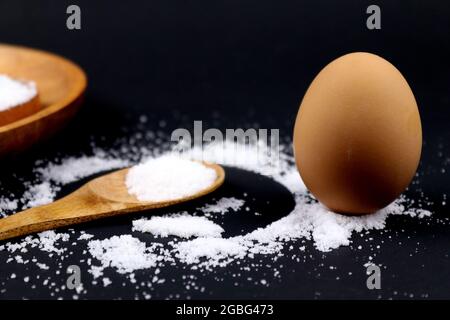 Stehendes Ei auf Salz und Holzlöffel auf schwarzem Hintergrund Stockfoto