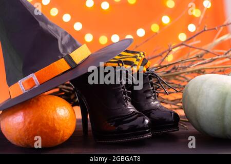 Hut, Stiefel, Strümpfe einer Hexe mit Ästen, Kürbisse auf orangefarbenem Hintergrund mit Bokeh. Halloween. Speicherplatz kopieren. Stockfoto