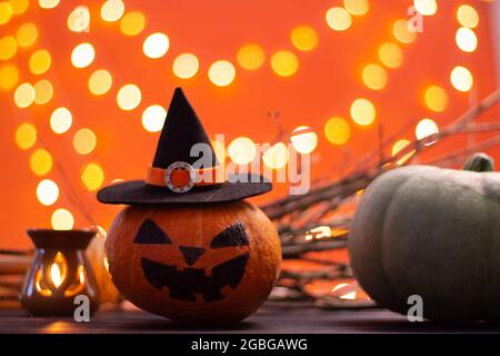 Hut einer Hexe mit Ästen, Kerze und Kürbissen auf orangefarbenem Hintergrund mit Bokeh. Halloween. Speicherplatz kopieren. Stockfoto