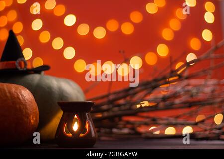 Hut einer Hexe mit Ästen, Kerze und Kürbissen auf orangefarbenem Hintergrund mit Bokeh. Halloween. Speicherplatz kopieren. Stockfoto