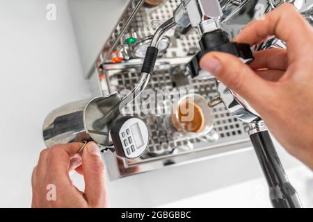 Barista macht Kaffee Dampfgaren von Milch mit einer Dampfmaschine im Café-Restaurant und überprüft die Temperatur mit einem Thermometer während des Aufschäumens im Krug Stockfoto