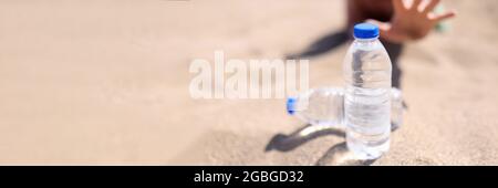 Der Mensch greift nach einer Wasserflasche, die auf Sand steht Stockfoto