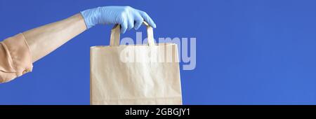 Kurier hält Gummihandschuhe mit Papiertüte auf blau Hintergrund Stockfoto