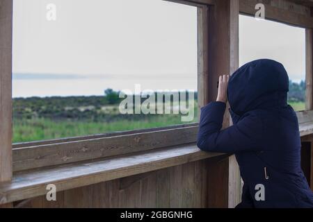 Frau mit Kapuze beobachtet Flamingos mit Ferngläsern in der Lagune von Fuente de Piedra, Malaga, Spanien Stockfoto