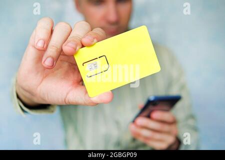 Ein Mann hält eine gelbe SIM-Karte und ein Mobiltelefon in der Hand. Freier Platz für Design und Text Stockfoto