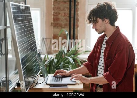 Junge Designerin sitzt am Tisch und arbeitet online am Laptop im Büro Stockfoto