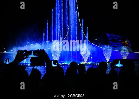 Die Menschenmenge fasziniert mit der Show des musikalischen Brunnens Silhouetten von Menschen von hinten werden am Telefon gefilmt Stockfoto