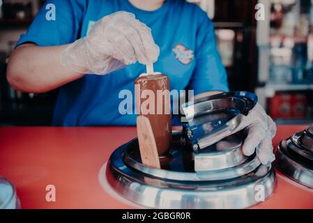 Ein Eisverkäufer taucht einen Popsicle in flüssige Schokolade. Stockfoto