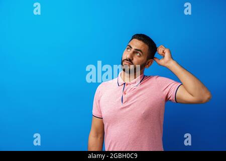 Nachdenklicher junger arabischer Mann, der vor blauem Hintergrund denkt und aufschaut Stockfoto