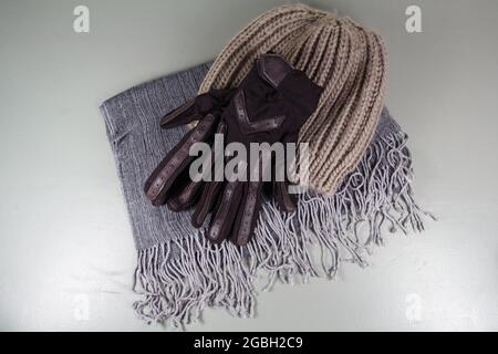 Grauer Schal aus Baumwolle, braune Handschuhe aus Baumwolle und Leder und beige Mütze aus Wolle Stockfoto