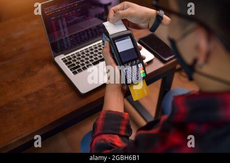 Mann, der an einem Tisch sitzt und eine kontaktlose Zahlung mit einem Kreditkartenleser abgibt Stockfoto