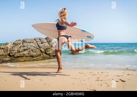 Frau mit einem Surfbrett, die am Strand in der Luft springt, Punta Paloma Beach, Tarifa, Cadiz, Andalucia, Spanien Stockfoto