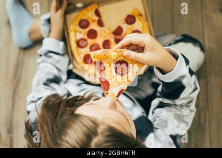 Draufsicht auf Mädchen Teenager, die zu Hause auf dem Boden sitzen und Pizza Pepperoni zu Mittag essen. Konzept des Lebensstils Stockfoto