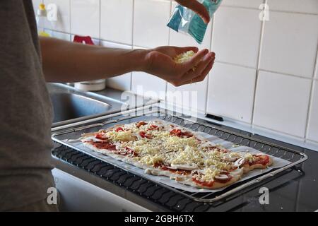 Ein Mann, der Käse auf Pizza legt und in der Küche kocht Stockfoto