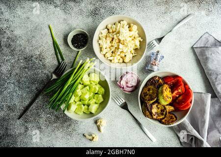 Gesunde Gemüseschale mit Zucchini, Tomaten, Gurken, Blumenkohl, Frühlingszwiebeln, Rote Zwiebel und Sesamsamen Stockfoto