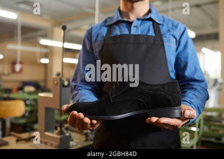 Arbeiter in der Schuhfabrik, die in der Werkstatt steht und einen neuen schwarzen Wildlederstiefel in der Hand hält Stockfoto