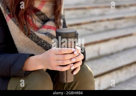 Frau mit Thermobecher in den Händen sitzt auf Stufen. Nahaufnahme Stockfoto