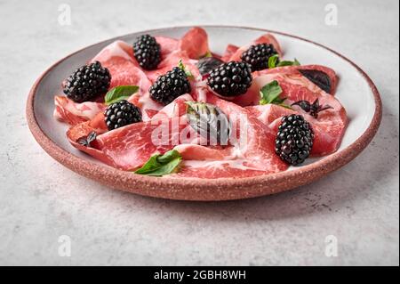 Scheiben Schinken coppa di parma Schinken mit Basilikum und Brombeere auf Keramikplatte. Selektiver Fokus, Nahaufnahme Stockfoto