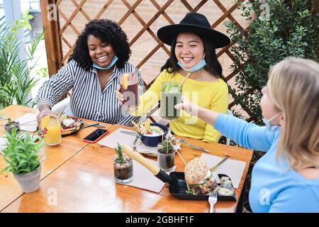 Fröhliche, vielfältige junge Freunde, die im Brunch-Restaurant mit Sicherheitsmasken essen - konzentrieren Sie sich auf das asiatische Mädchengesicht Stockfoto