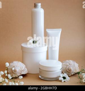 Set natürliche Schönheit kosmetische Hautpflegeprodukte mit Blumen Muscheln auf beigem Hintergrund. White Kit Creme Glas Tube kosmetische Produkte für Körper Stockfoto