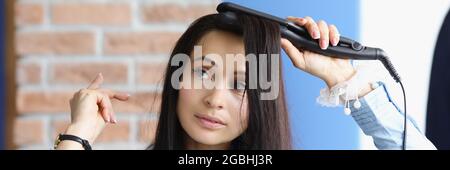 Brünette Frau macht Locken ihrer Haare mit Lockenstab Stockfoto