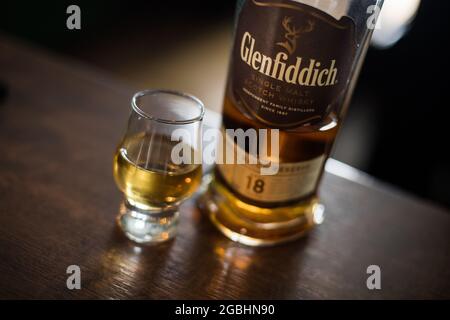 Bukarest, Rumänien - 5. August 2021: Illustrative redaktionelle Aufnahme einer Glenfiddich-Whisky-Flasche mit Single Malt-Malt-Schottenstoff neben einem Glas auf der Theke in einer pu Stockfoto