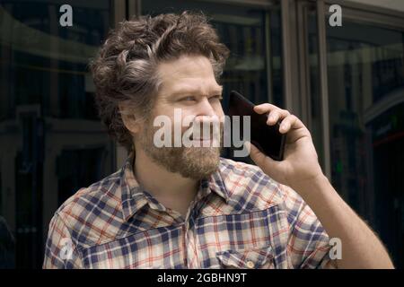 nordischer Mann mit Bart und Lächeln im Gespräch auf dem Handy auf der Straße Stockfoto