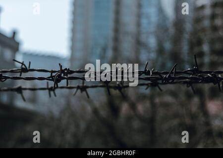 Rostiger Stacheldraht auf einem unscharfen dunklen urbanen Hintergrund. Pessimistische Szene. Stockfoto